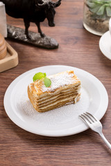Slice of layered honey cake with mint leaves on wooden table