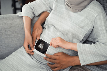 gesture of couple's hand hold at ultrasound on pregnant belly when sitting on the couch