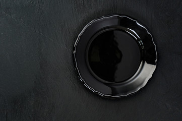 Empty rustic black plate on dark stone background, copy space, top view