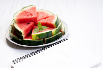 Slices of fresh watermelon with notebook paper on white wooden background