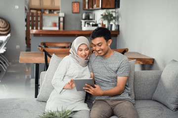 muslim pregnant woman using tablet pc with husband in livingroom