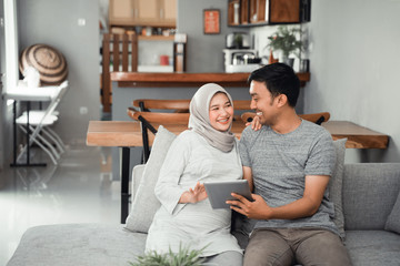muslim pregnant woman using tablet pc with husband in livingroom
