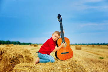 Naklejka na ściany i meble Romantic boy with a guitar in the field . fashionable little musician in nature . children's music education