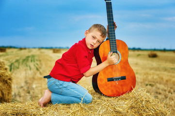 Naklejka na ściany i meble Romantic boy with a guitar in the field . fashionable little musician in nature . children's music education