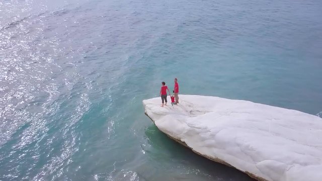 aerial view of family recreation on white stone cape in Kalymnos or Governor Beach in Cyprus, father mother and son in red shirt have fun on sea coast, people traveling, drone camera fly around   