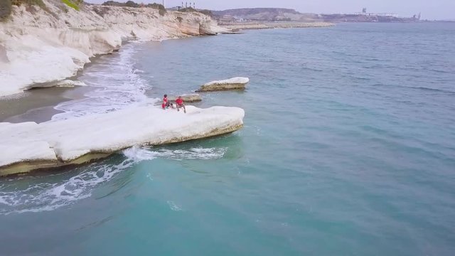 aerial view of family on white stone cape in Kalymnos or Governor Beach in Cyprus, father mother and son in red shirt sits on sea coast, traveling and vacation, drone camera fly 