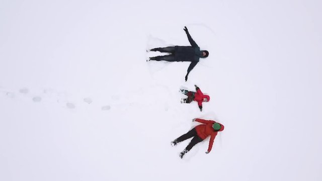 happy family having fun, mother father and son lies on snow and makes snow angel, winter vacation   