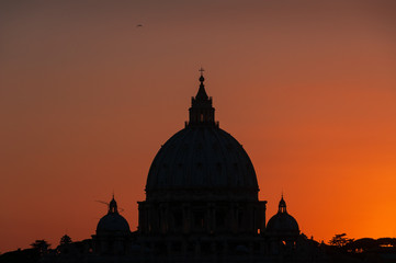 Dark silhouette of the dome of St Peters Basilica against bright red sunset sky