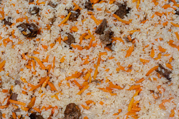 Close-up view of Eastern tasty food background. Traditional Asian culinary dish - pilaf. Ingredients: rice with slices of meat, fat and vegetables (carrot, garlic), spices- popular recipe.
