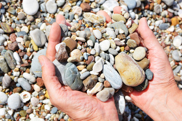 Men's tanned hands holding in the palms of beautiful sea stones on the beach