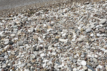 Multi-colored large sea pebbles of various shapes on the sandy shore of the Mediterranean sea for background