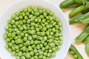 Fresh green peas in white plate on wooden table