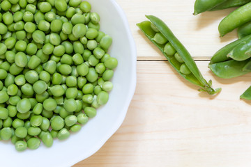 Freshly harvested green sugar peas in white plate on wooden table