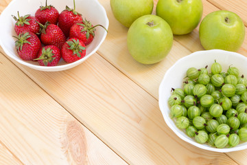 Naklejka na ściany i meble Green apples, gooseberry and red strawberries in white bowles on light wooden table