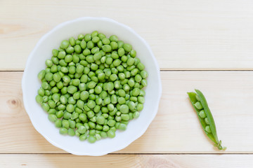 Green pease ready to eat on white plate on light wooden table