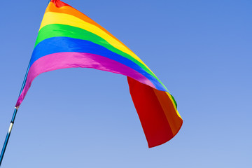 Gay rainbow flag waving in the wind in a clear blue sky