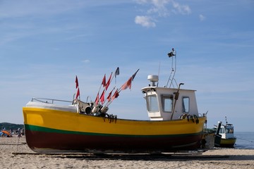 Wooden fishing boat on the beach of Baltic Sea in Sopot/Poland in sunny summer day. Red flag poles for marking networks. 