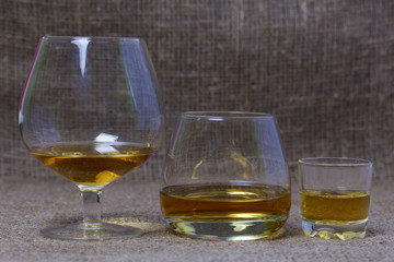 Glasses and a stack with a strong alcoholic beverage poured into them. Stand in a row. Against the backdrop of coarse linen fabric. Close-up.