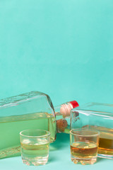Bottled bottles of strong alcohol. From transparent glass, a square form. Near the stack with a drink poured. Against the background of mint color.