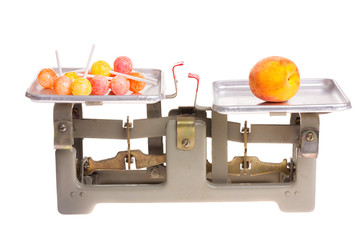 Healthy VS unhealthy. Old metal weighs with candy and fruit isolated on white background.