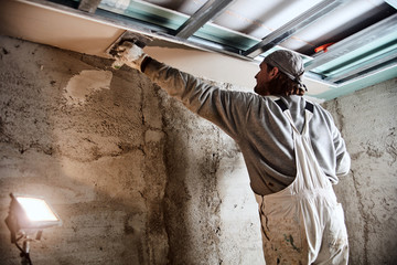 Construction worker plastering gypsum walls inside the house.