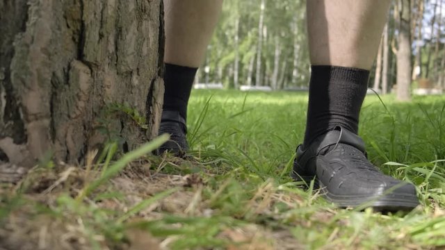 men's feet in shoes treading near tree. man is hiding behind tree in park.