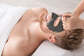 Cosmetologist applying mask on man's face in spa salon
