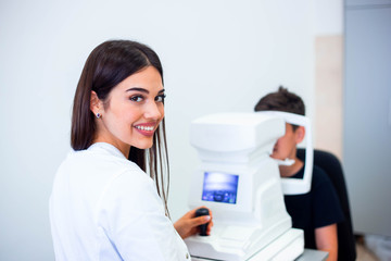Female oculist using machine for checking eye sight in clinic. Little boy looking at equipment and doctor testing eye pupil in optical store. Concept of eye care and health.