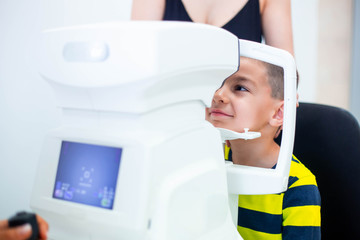 Female oculist using machine for checking eye sight in clinic. Little boy looking at equipment and doctor testing eye pupil in optical store. Concept of eye care and health.