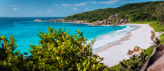 Panorama of epic Grand Anse Beach in La Digue island, Seychelles. White sand beach, big ocean waves and unique granite rocks along coastline. Summer vacation and holiday travel concept