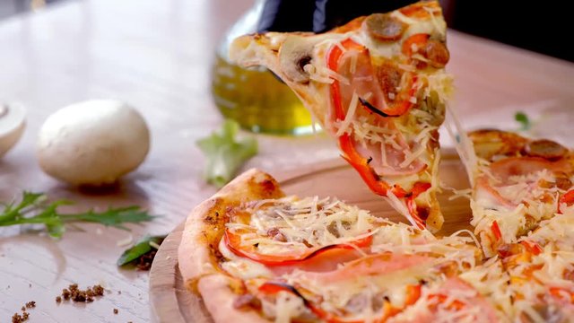 Cook takes a slice of bacon, mushroom and cheese pizza. Hand in rubber glove close-up