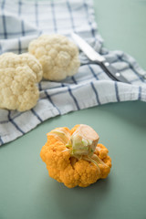 Bunter Blumenkohl Orange und Weiß auf Geschirrtuch mit Messer auf Pastell Grün Hintergrund