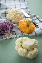 Bunter Blumenkohl in Lila, Orange und Weiß auf Geschirrtuch mit Messer auf Pastell Grün Hintergrund