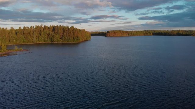 Aerial footage of a lake in a Swedish forest during sunset. Flying forward over the lake towards the end of it.