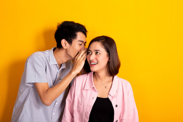 man whispering to a woman about gossip, woman looked shocked shoot over yellow background