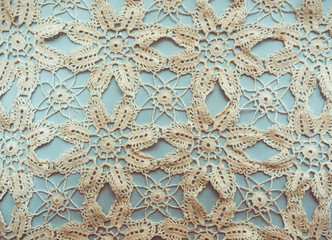Hand knitted traditional lace mat doily isolated on light blue background, vintage photo effect.