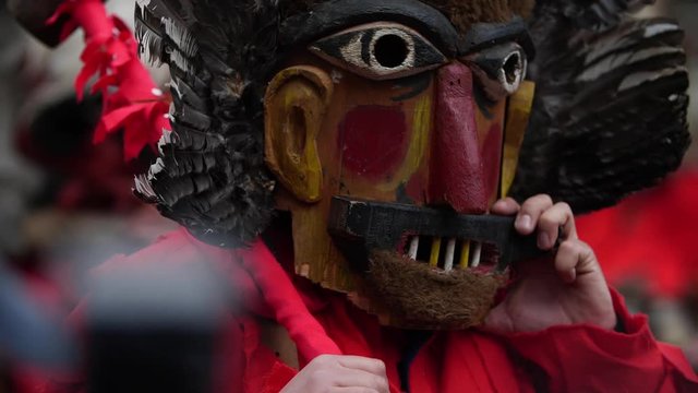 Bulgarian kuker with a dull nose wooden mask followed by another wooden mask with real chicken feathers as decoration.