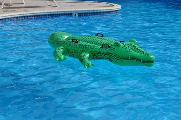 A green crocodile plastic pool float on a sandy beach