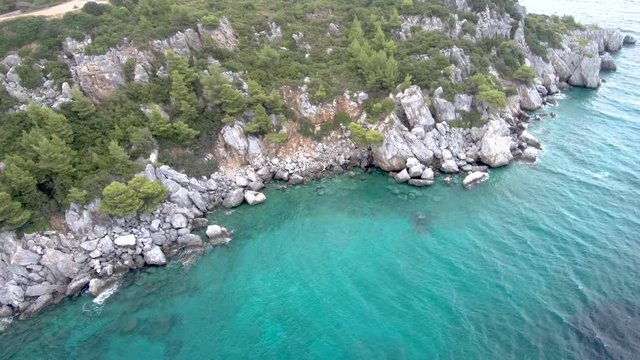 Aerial view of steep rocks in turquoise crystal sea in the area of Agia Paraskevi Halkidiki, Greece, circular movement by drone