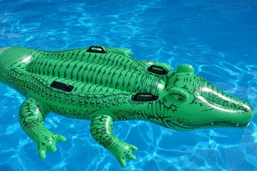 A green crocodile plastic pool float on a sandy beach