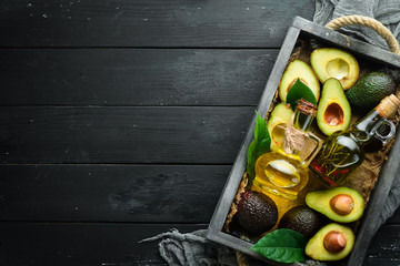 Avocado oil and fresh avocados on a black background. Rustic style. Top view. Free space for your text.