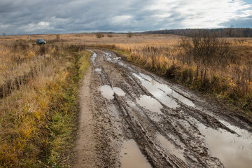 Country road rut with puddles through agricultural field