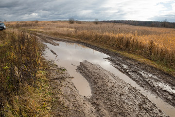 Country road rut with puddles through agricultural field