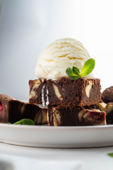 Chocolate brownie with vanilla ice cream, rasberry and mint on a white background. Copy space.