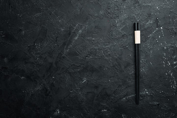 Wooden chopsticks on a black stone background. Top view. Free space for your text.