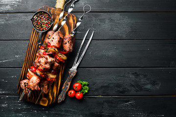 Shish kebab BBQ meat with onions and tomatoes. On a black background. Top view. Free space for your...