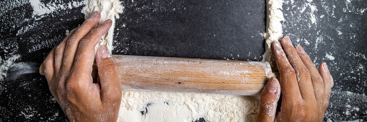 Female hands keep rolling pin with flour on dark table. Baking background. Flour, cooking and bake...