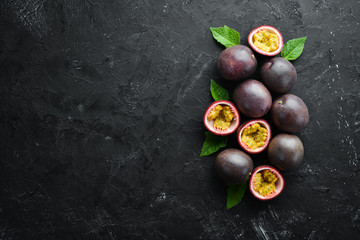 Passion fruits with leaves on a black background. Tropical Fruits. Top view. Free space for text.