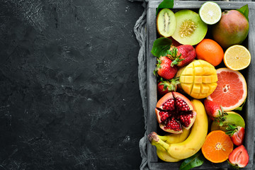 Fruits in a wooden box. Citrus, melon, pomegranate, strawberry, banana. Top view. Free space for your text.