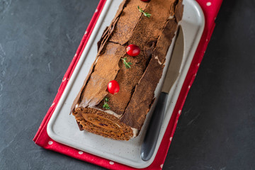 Buche de Noel. Traditional Christmas dessert, Christmas yule log cake with chocolate cream, cranberry. On stone gray background with Christmas tree branches.